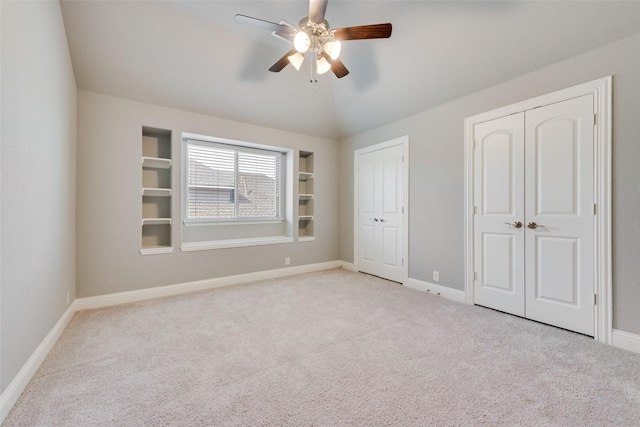 unfurnished bedroom with light carpet, vaulted ceiling, baseboards, and multiple closets