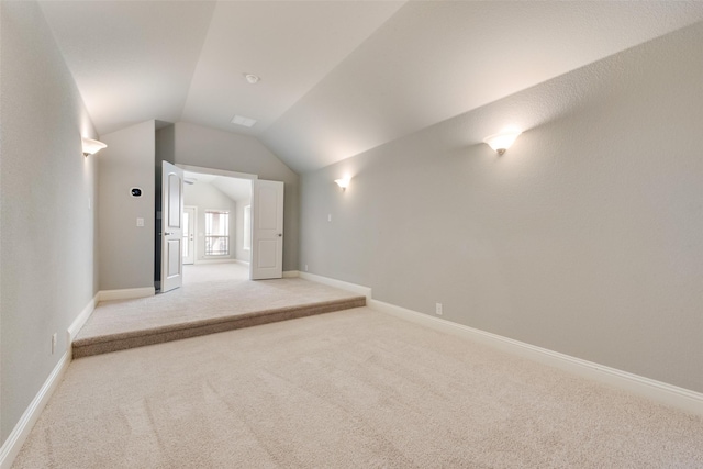 spare room featuring light carpet, vaulted ceiling, and baseboards