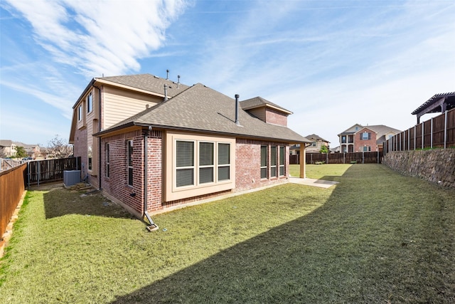 back of property featuring a shingled roof, a fenced backyard, a yard, central air condition unit, and brick siding