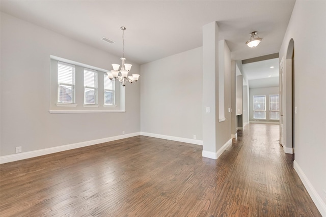 spare room featuring dark wood-type flooring, visible vents, baseboards, and an inviting chandelier