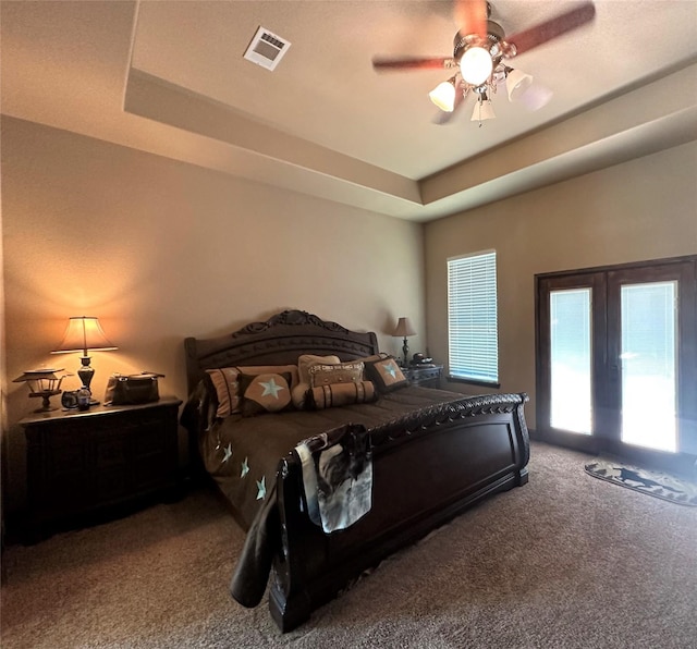 carpeted bedroom with a ceiling fan, a raised ceiling, and visible vents