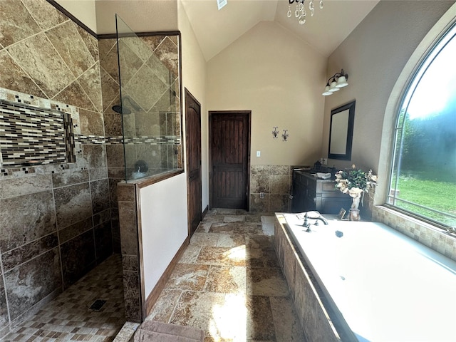 full bath with vanity, vaulted ceiling, walk in shower, stone tile flooring, and a bath