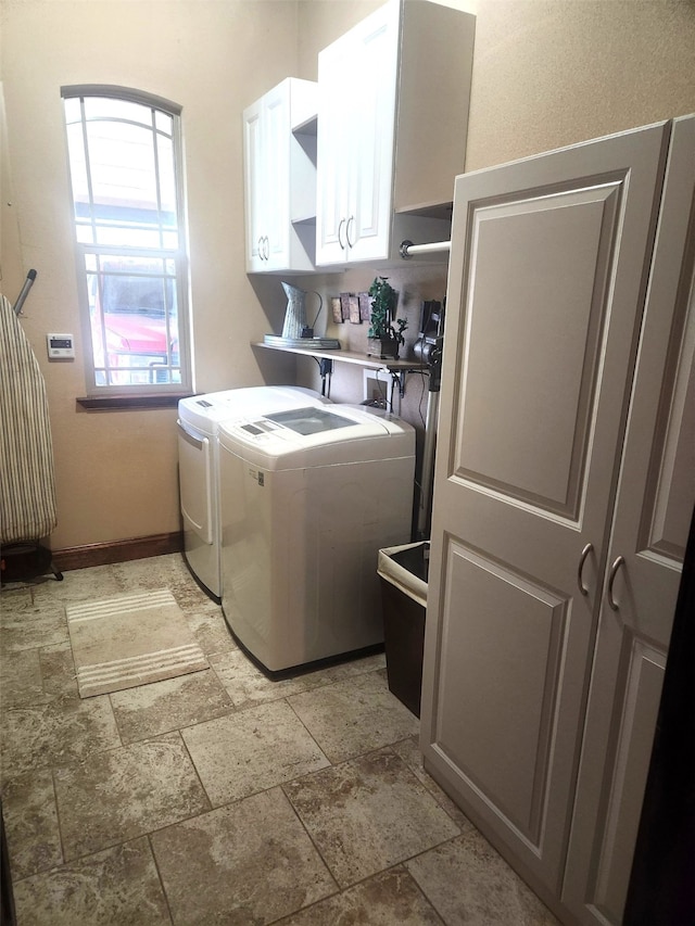 clothes washing area with stone finish flooring, cabinet space, independent washer and dryer, and baseboards