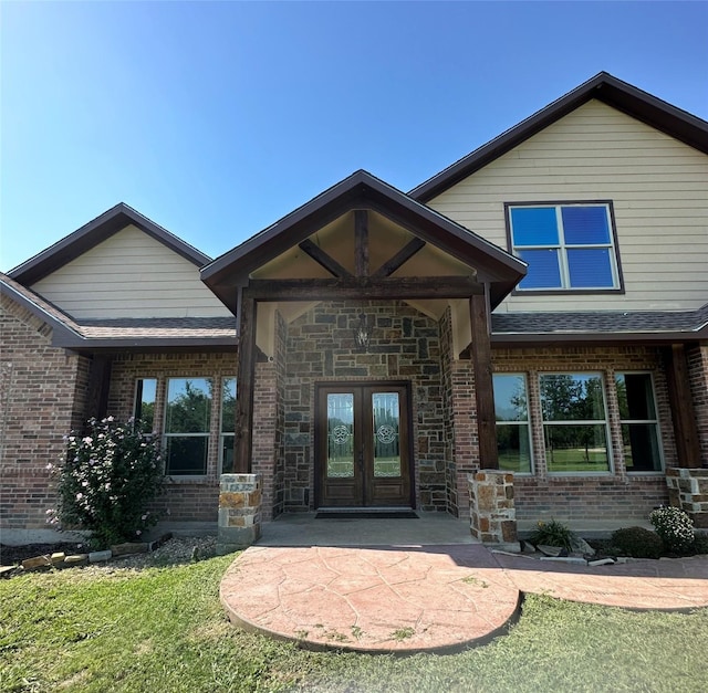 entrance to property with stone siding, french doors, a shingled roof, and brick siding