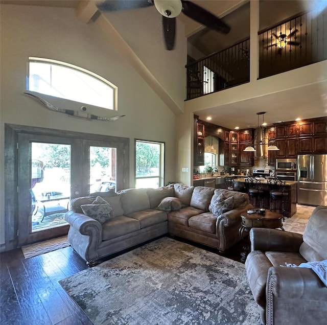 living area featuring light wood-type flooring, a towering ceiling, beam ceiling, and a ceiling fan