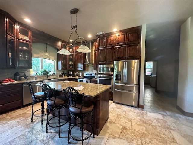 kitchen with light stone counters, stainless steel appliances, a kitchen island, decorative backsplash, and stone tile flooring