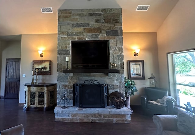 living area featuring a stone fireplace, wood finished floors, and visible vents