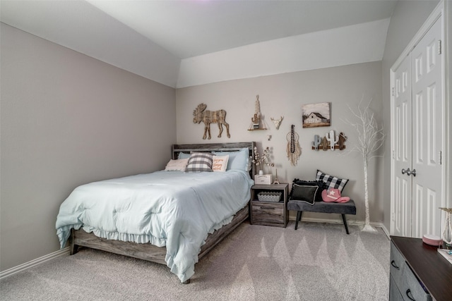 bedroom featuring a closet, light colored carpet, vaulted ceiling, and baseboards