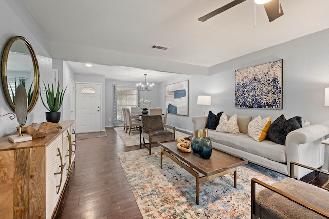 living room featuring dark wood-type flooring, ceiling fan with notable chandelier, visible vents, and baseboards