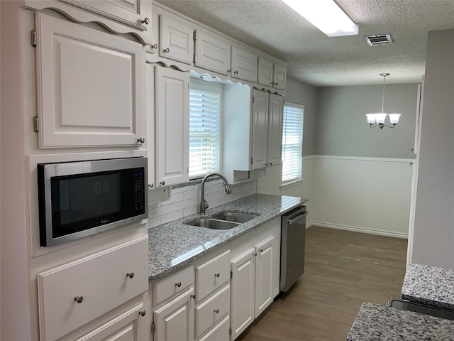 kitchen featuring visible vents, white cabinets, decorative light fixtures, stainless steel appliances, and a sink