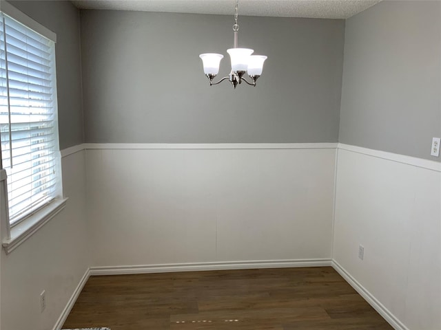 empty room with dark wood-style floors, a textured ceiling, and an inviting chandelier