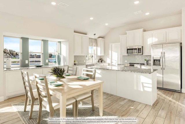 kitchen with appliances with stainless steel finishes, pendant lighting, white cabinetry, and a kitchen island