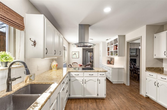 kitchen with dark wood-style floors, island exhaust hood, white cabinetry, a sink, and a peninsula