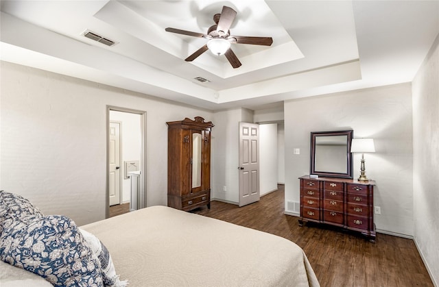 bedroom featuring dark wood-style floors, visible vents, and a tray ceiling