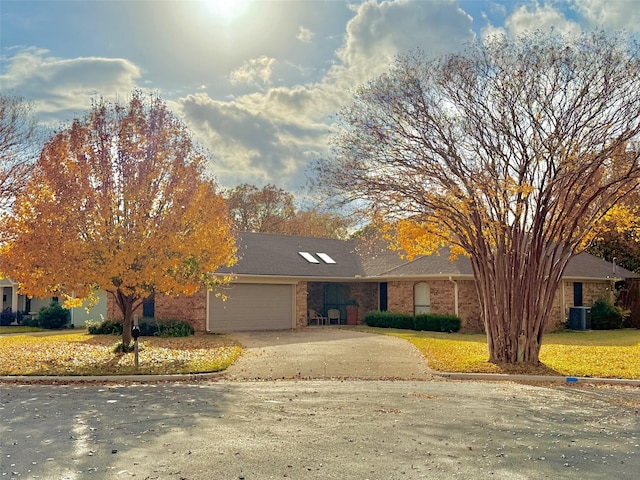 view of front of property featuring brick siding, concrete driveway, an attached garage, central AC, and a front yard