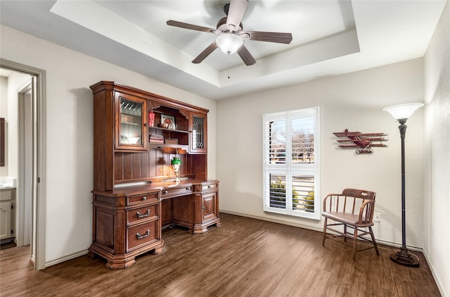 office area featuring a tray ceiling, dark wood finished floors, baseboards, and ceiling fan