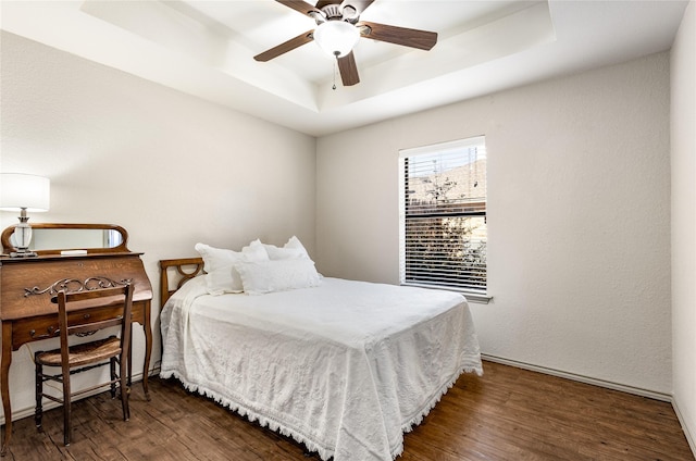 bedroom with a ceiling fan, a tray ceiling, and wood finished floors