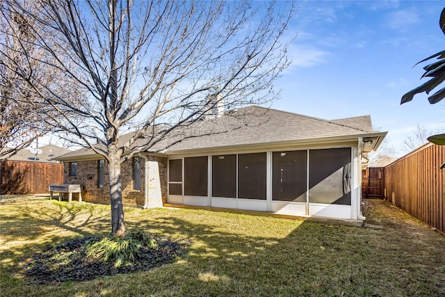 back of property with a sunroom, a fenced backyard, roof with shingles, and a yard