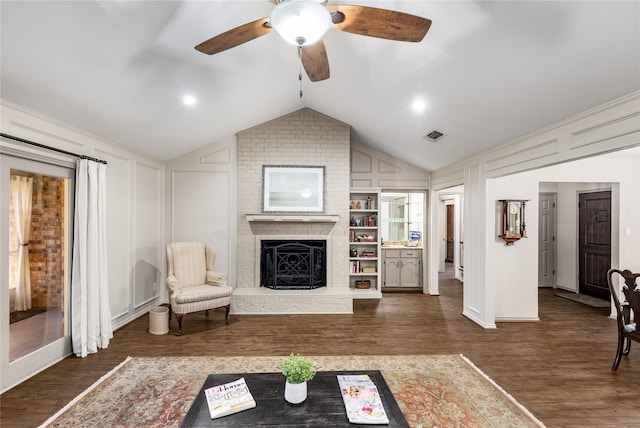 living room featuring lofted ceiling, ceiling fan, a decorative wall, wood finished floors, and a brick fireplace