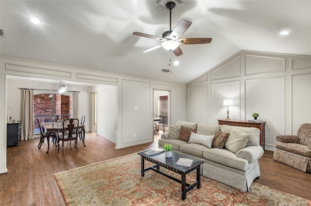 living room with lofted ceiling, ceiling fan, a decorative wall, wood finished floors, and visible vents