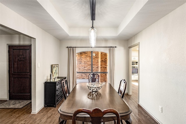 dining space featuring baseboards, a raised ceiling, dark wood-style flooring, and a textured wall