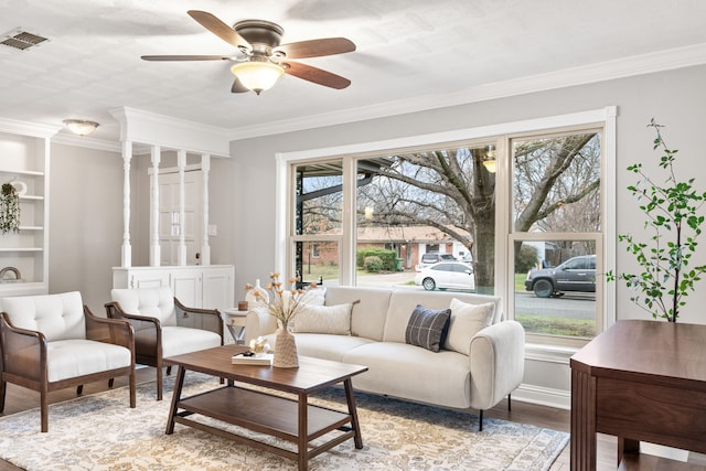 living room featuring built in features, crown molding, visible vents, ceiling fan, and wood finished floors