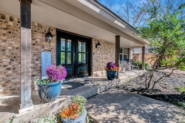 property entrance featuring a porch, fence, french doors, and brick siding