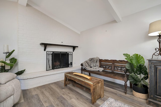 living area featuring lofted ceiling with beams, a brick fireplace, and wood finished floors