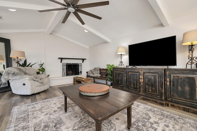 living room with lofted ceiling with beams, ceiling fan, a fireplace with raised hearth, and wood finished floors