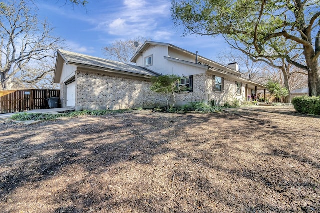 view of property exterior featuring an attached garage, a chimney, and brick siding