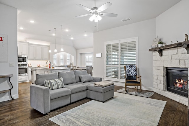 living area featuring a fireplace, visible vents, baseboards, a ceiling fan, and dark wood-style floors