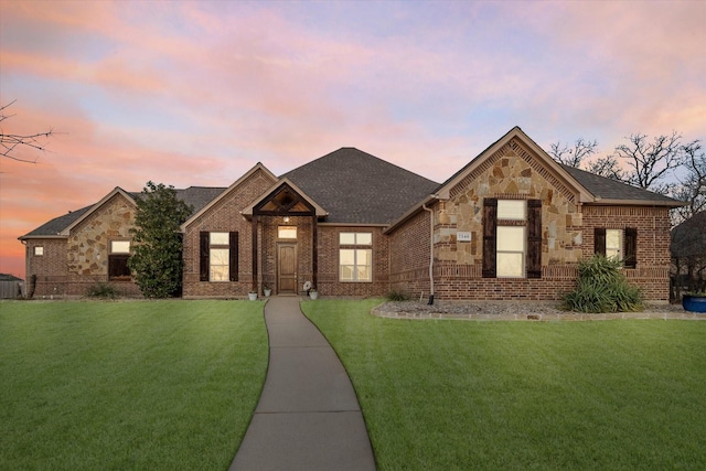 view of front of property with stone siding, a shingled roof, a lawn, and brick siding