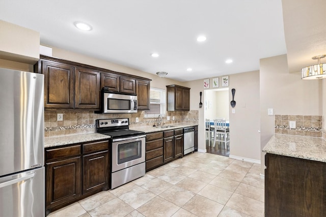 kitchen with light stone countertops, appliances with stainless steel finishes, dark brown cabinets, and a sink