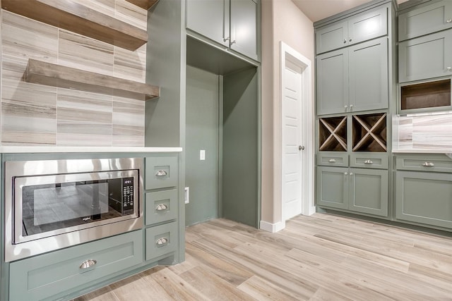 kitchen featuring light countertops, stainless steel microwave, green cabinetry, and light wood finished floors