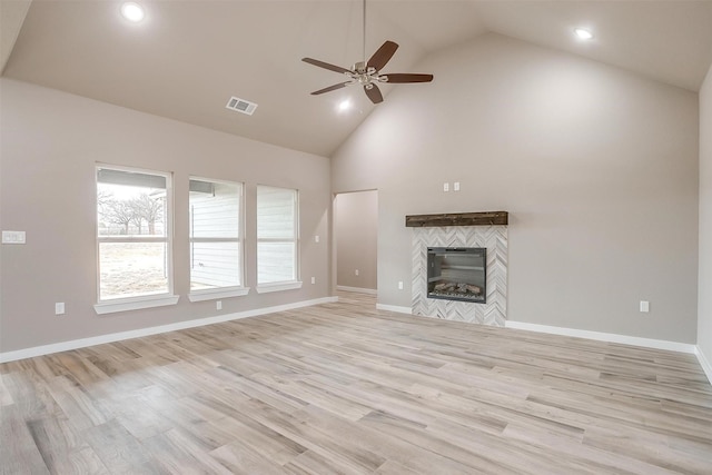 unfurnished living room with visible vents, baseboards, a tiled fireplace, light wood-style flooring, and high vaulted ceiling