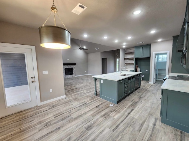 kitchen with a fireplace, visible vents, hanging light fixtures, a kitchen island with sink, and a sink