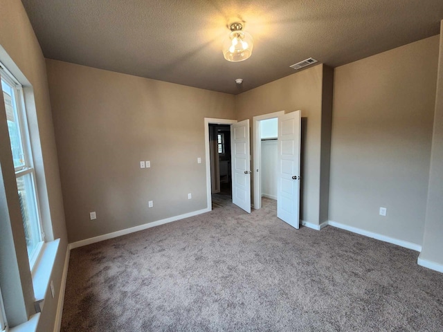 unfurnished bedroom with carpet floors, visible vents, a textured ceiling, and baseboards