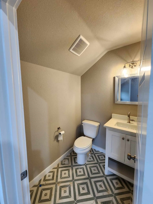 half bath with lofted ceiling, toilet, vanity, visible vents, and baseboards