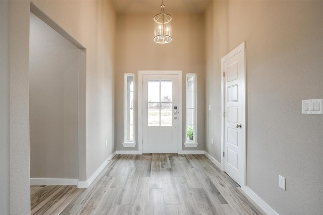 foyer entrance with light wood-type flooring, a high ceiling, a notable chandelier, and baseboards