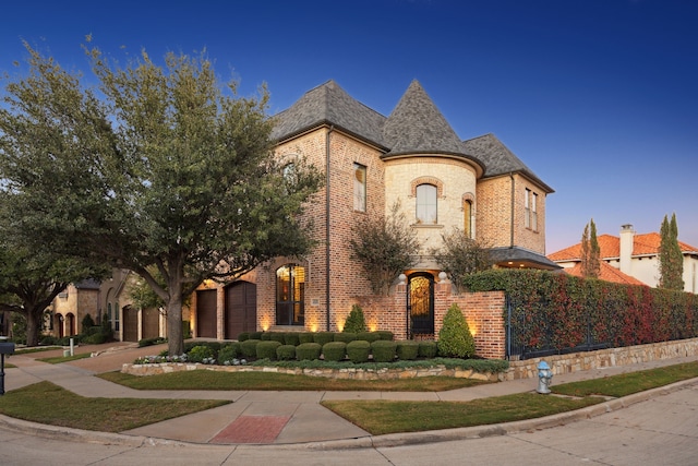 french country style house with driveway, brick siding, an attached garage, and a shingled roof