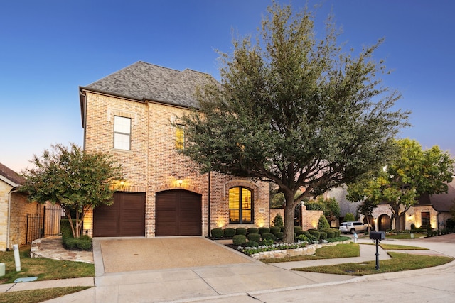 french provincial home with an attached garage, driveway, brick siding, and a shingled roof