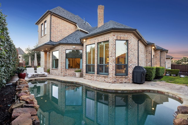 back of property at dusk with a patio, brick siding, a chimney, and a fenced in pool