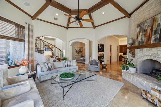 living room with beamed ceiling, a stone fireplace, and a towering ceiling