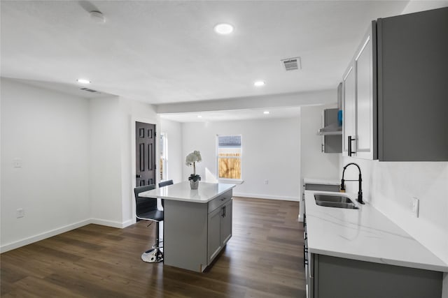 kitchen with gray cabinetry, a sink, visible vents, a kitchen breakfast bar, and a center island