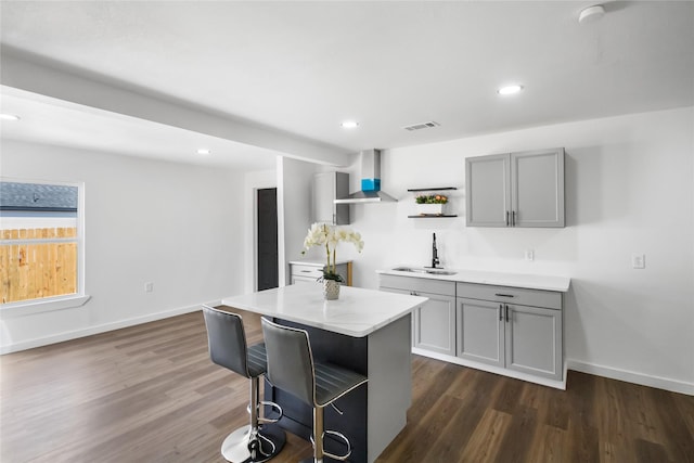 kitchen with dark wood-style floors, open shelves, gray cabinetry, a sink, and wall chimney exhaust hood