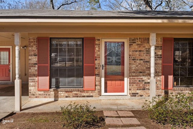 view of exterior entry with brick siding and roof with shingles