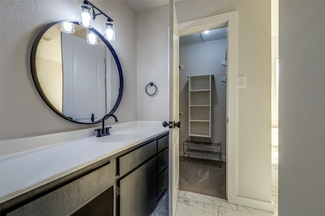 bathroom featuring marble finish floor, a walk in closet, vanity, and baseboards