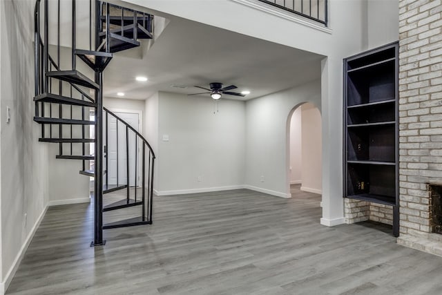 interior space featuring arched walkways, baseboards, a ceiling fan, stairway, and wood finished floors