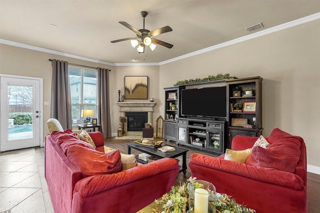 living area with a glass covered fireplace, visible vents, crown molding, and baseboards