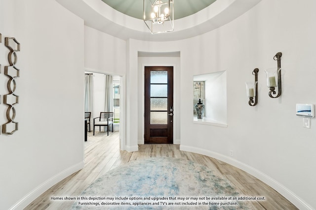 entryway with light wood-style floors, a raised ceiling, baseboards, and an inviting chandelier